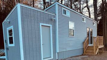 A two-story shed with a door and windows, a wooden deck, and a staircase leading to a porch.