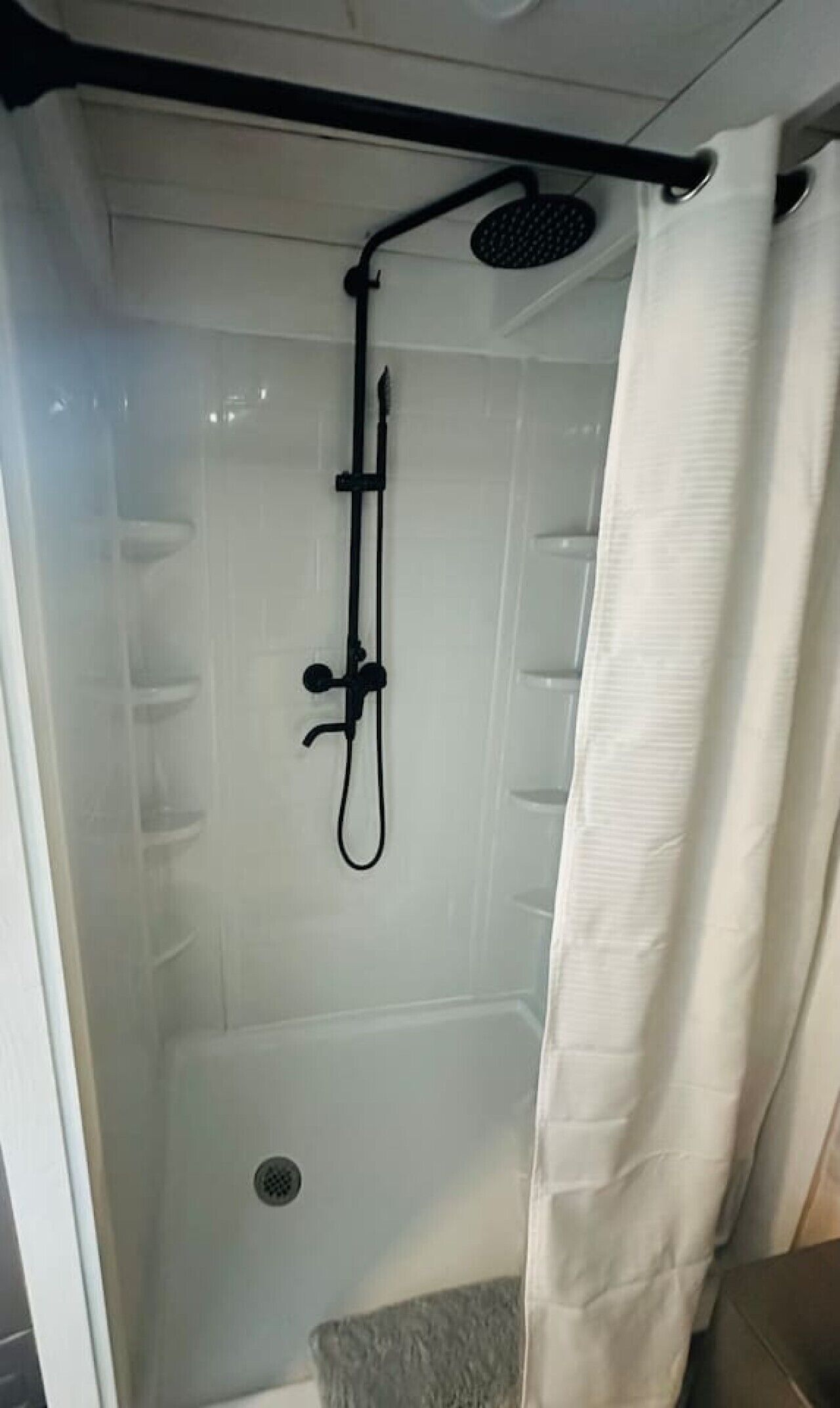 A glass-enclosed shower stall with a black showerhead and a white curtain.