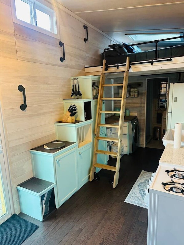 A compact kitchen with a lofted sleeping area, built-in cabinets, and a ladder for access.