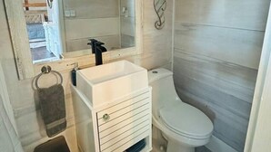 Kylpyhuone, jossa on valkoinen pesuallas, wc ja peili.