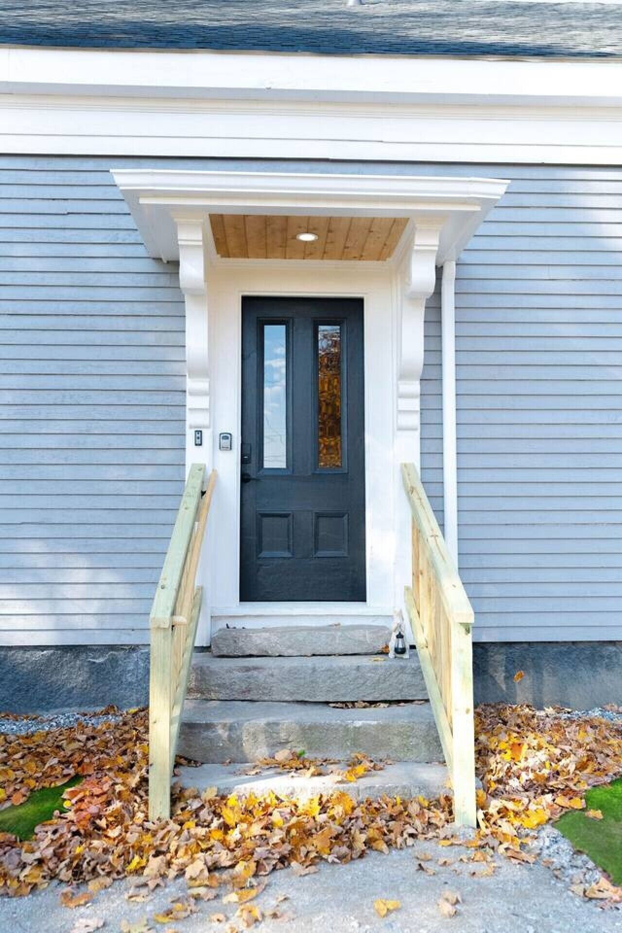 A front door with a dark-colored door, a white porch with a wooden handrail, and a stone step leading up to the door.