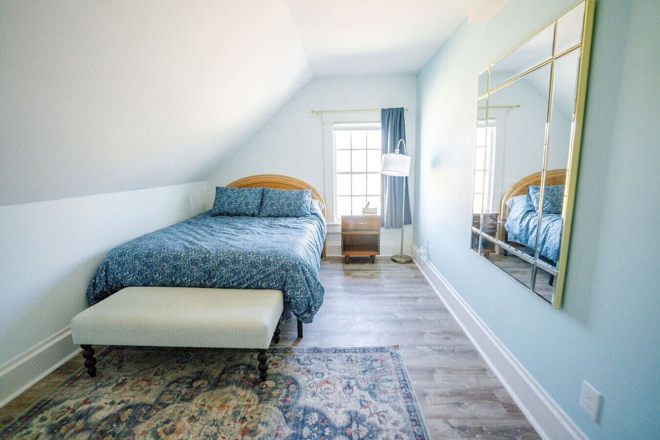 A bedroom with a bed, bench, rug, and a large mirror.