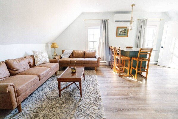 Een woonkamer met een bruine bank, een salontafel, en een eethoek met houten stoelen en een tafel.
