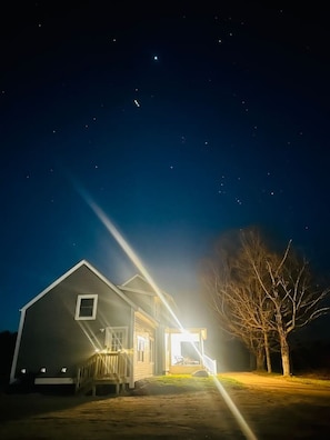 Una casa amb un porxo i un arbre al davant, sota un cel estrellat.