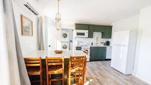 A modern kitchen with green cabinets, a white refrigerator, and a dining area with wooden chairs and a white table.