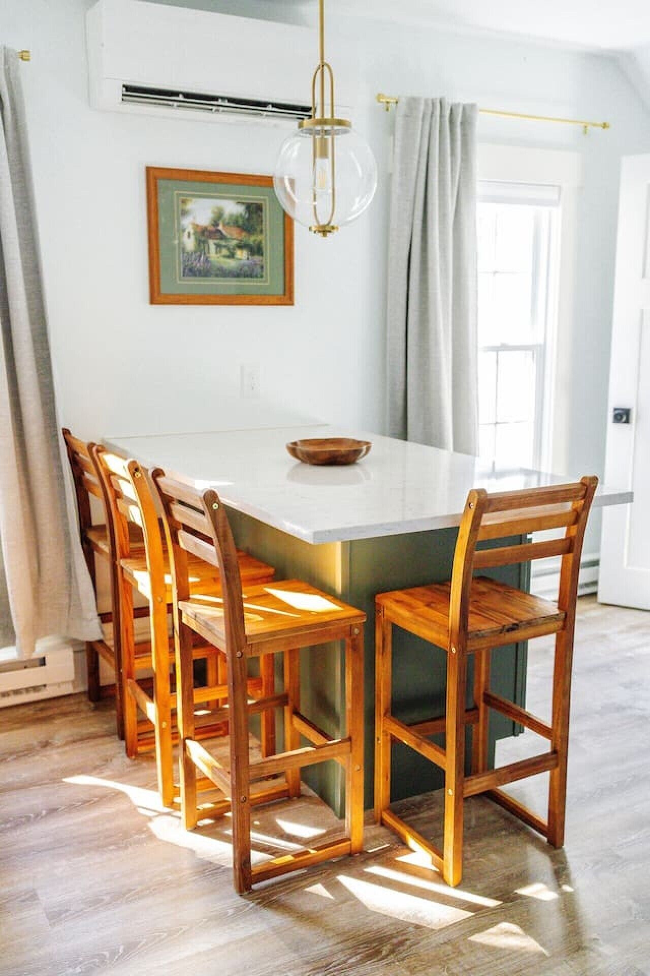 A dining area with a white island table surrounded by wooden chairs, a pendant light, and a framed picture on the wall.