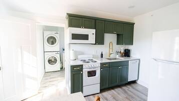 A compact kitchen with a washing machine, microwave, stove, and sink.