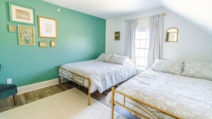 Une chambre avec deux lits, un mur vert et des tableaux encadrés.