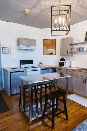 Une cuisine moderne dotée d’un îlot central, d’appareils électroménagers en acier inoxydable et d’un luminaire suspendu.