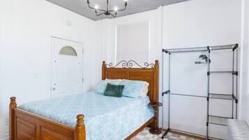 Ein Schlafzimmer mit einem hölzernen Bett, einem karierten Teppich, einem Wäscheständer aus Metall und einer weißen Tür.