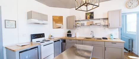 Una cocina moderna con una isla central, electrodomésticos de acero inoxidable y una lámpara colgante de diseño geométrico.