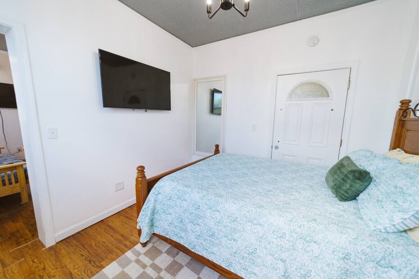 A bedroom with a bed, a television mounted on the wall, a door with an arched window, and a wooden floor.
