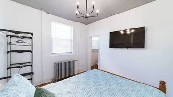 A bedroom with a bed, a radiator, a wall-mounted TV, and a window with blinds.