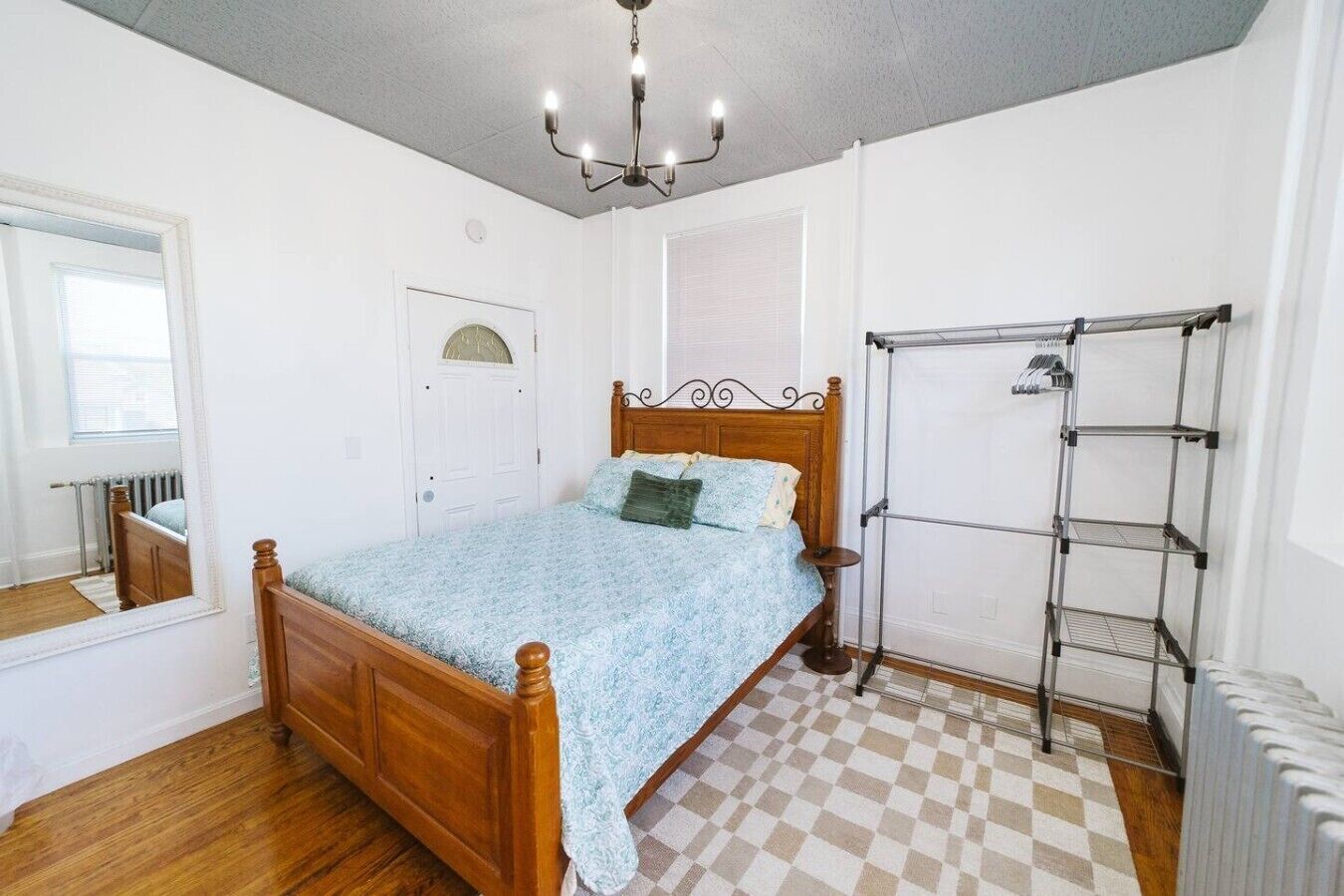 Ein Schlafzimmer mit einem hölzernen Bett, einem Heizkörper, einem karierten Boden und einem Wäscheständer aus Metall.