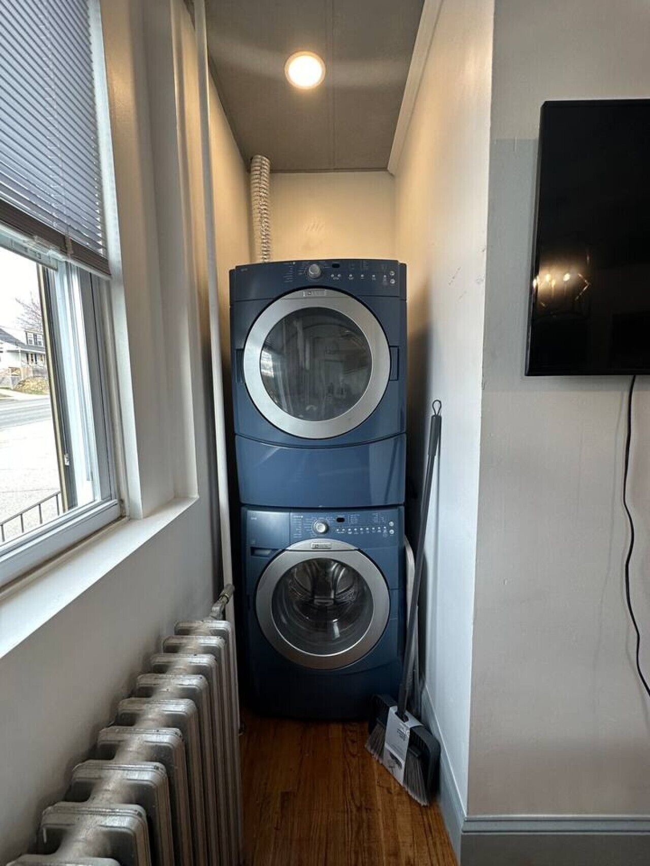 Un cuarto de lavado con lavadora y secadora apiladas, un radiador y un televisor montado en la pared.