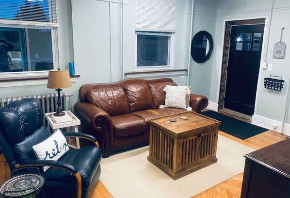 A living room with a brown leather sofa, a black leather armchair, a wooden coffee table, and a lamp.