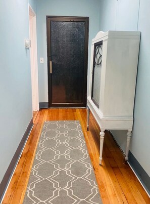 A hallway with a wooden floor, a patterned rug, a white cabinet, and a dark door.