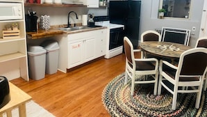 Cocina compacta con armarios blancos, un refrigerador negro y una zona de comedor con una mesa redonda y sillas.