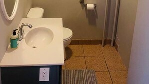Un baño pequeño con lavamanos blanco, espejo, inodoro y ventana sobre el inodoro.