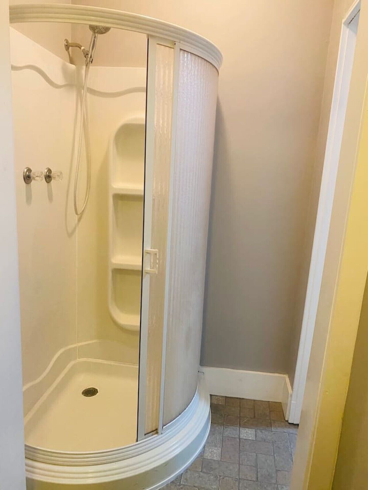 A corner shower with a glass door, a showerhead, and a small shelf.