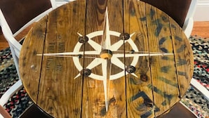 Una mesa redonda de madera con un diseño de brújula, rodeada de sillas blancas con cojines oscuros.