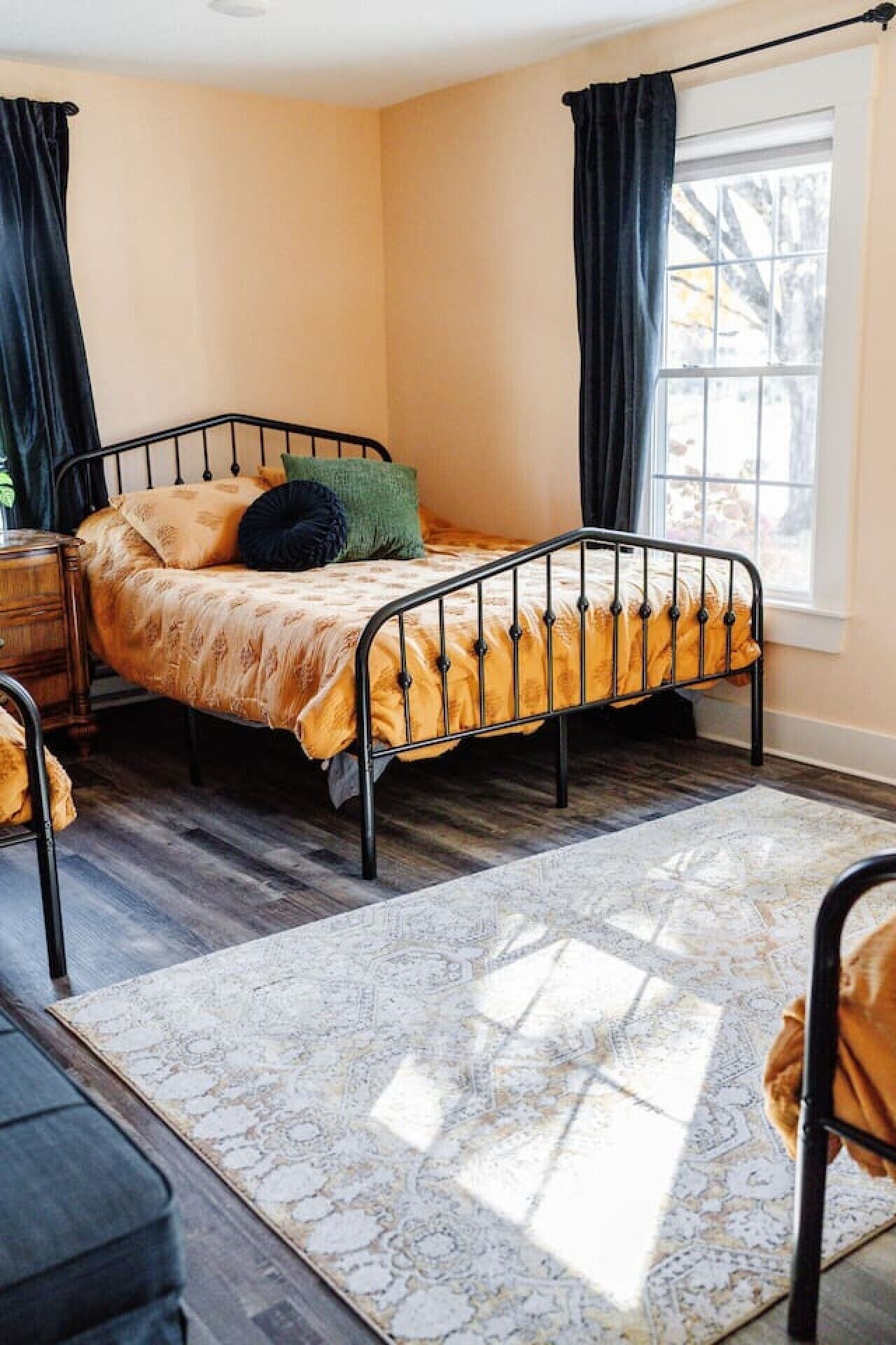 A single bed with a metal frame, a patterned rug, and a window with curtains.