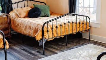 A single bed with a metal frame, a patterned rug, and a window with curtains.