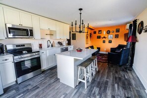A modern kitchen with stainless steel appliances, a central island, and a dining area with a dark-colored sofa.