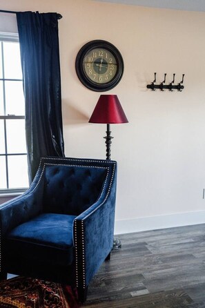 A room with a dark blue upholstered armchair, a red floor lamp, a wall clock, and a coat rack.