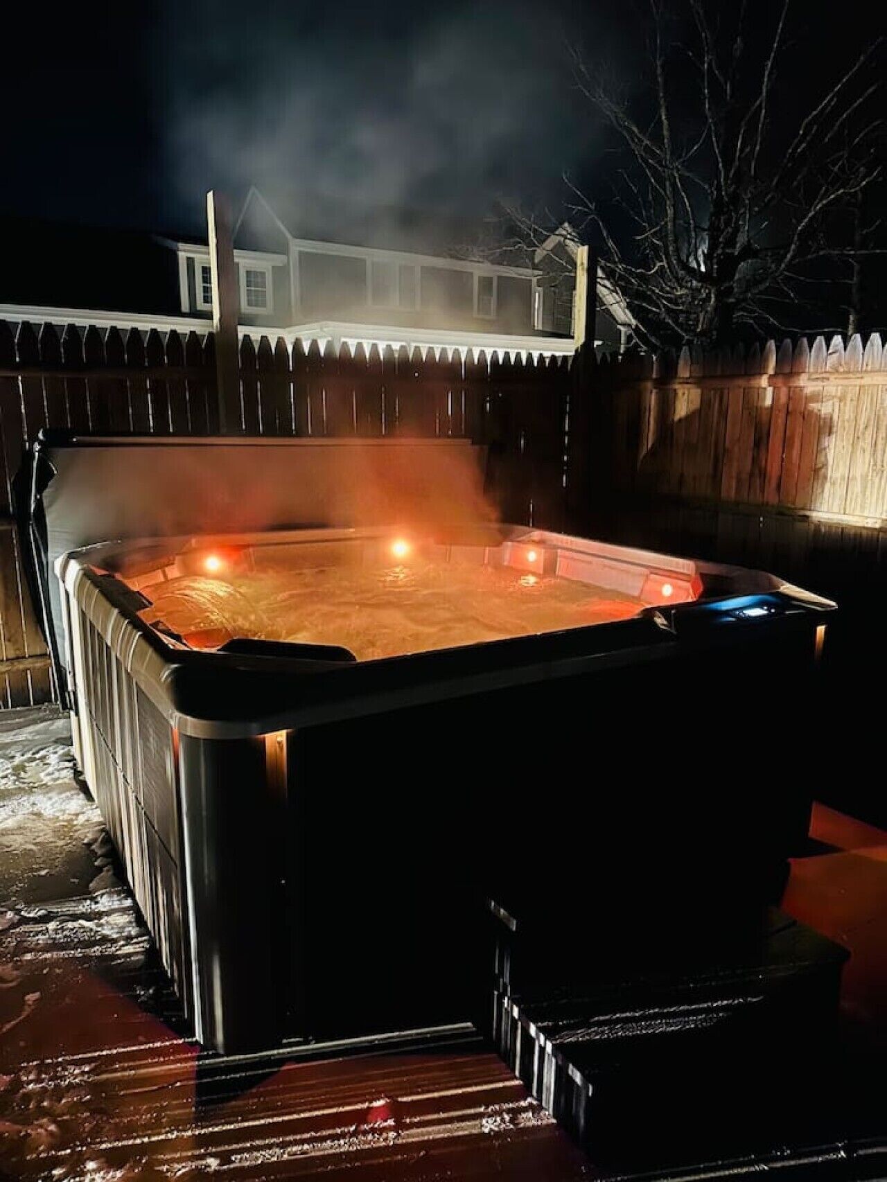 Ein Whirlpool im Freien bei Nacht, mit Holzzaun und einem Haus im Hintergrund.