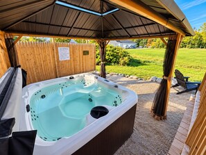 Un jacuzzi bajo una pérgola de madera, con un jardín césped al fondo.