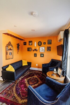A living room with a sofa, armchair, and a coffee table, featuring a patterned rug and wall decorations.