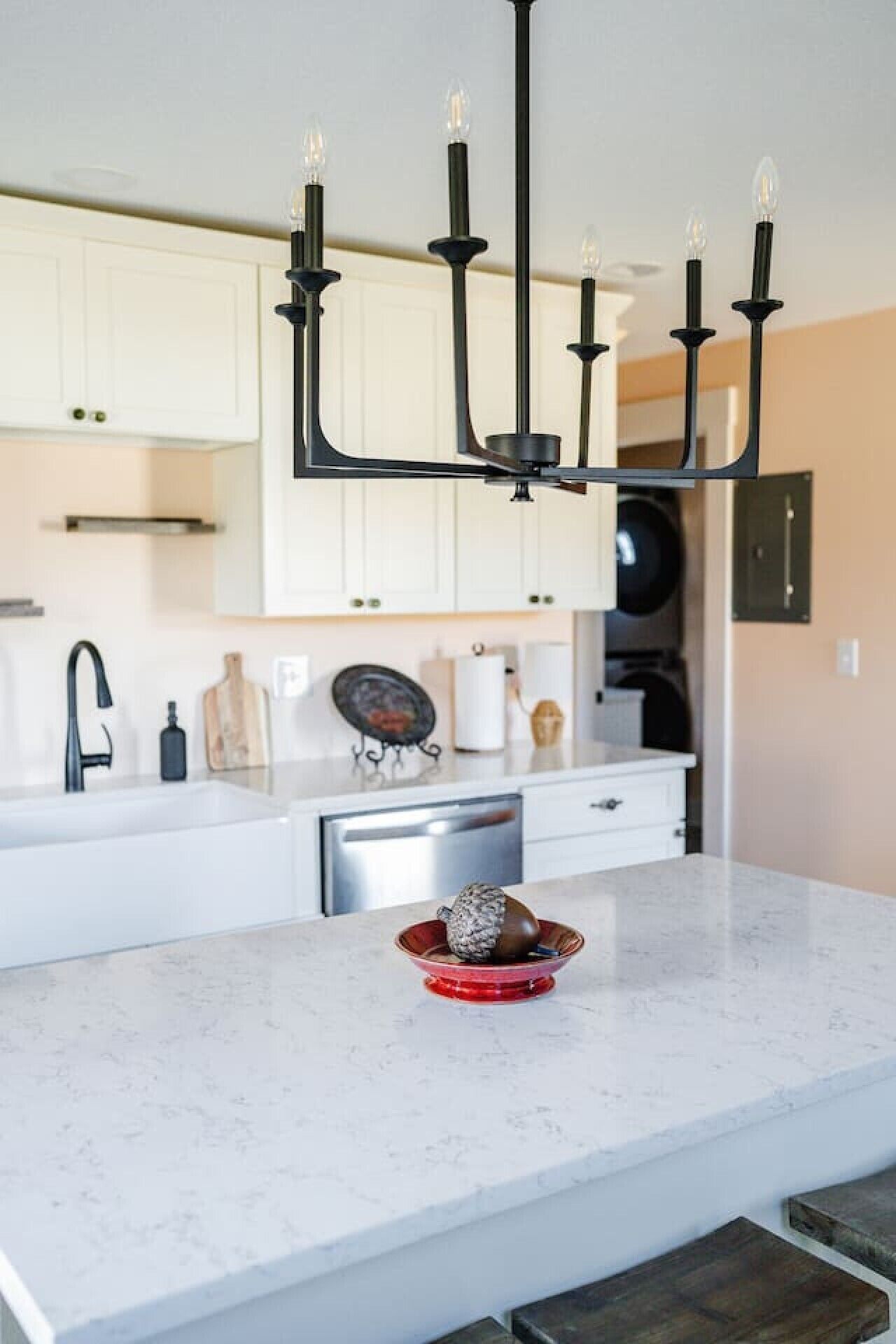 A modern kitchen with a white countertop, a black faucet, a dishwasher, and a red bowl with a decorative item.