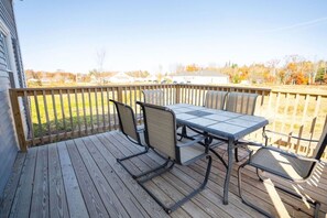 Une terrasse en bois avec une table et des chaises, donnant sur un quartier résidentiel avec des maisons et des arbres.