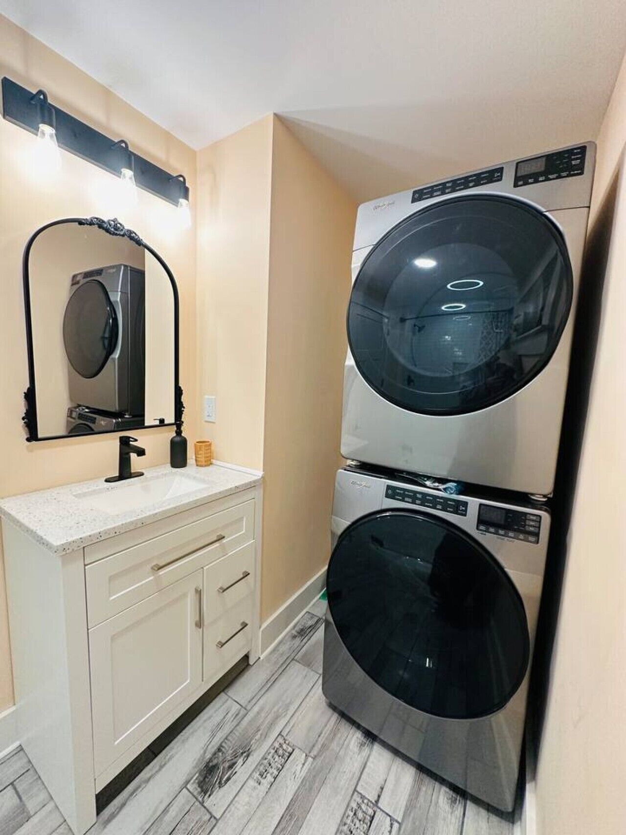 A compact laundry room with a washing machine and dryer stacked vertically, a sink with a mirror above it, and a light fixture above the mirror.