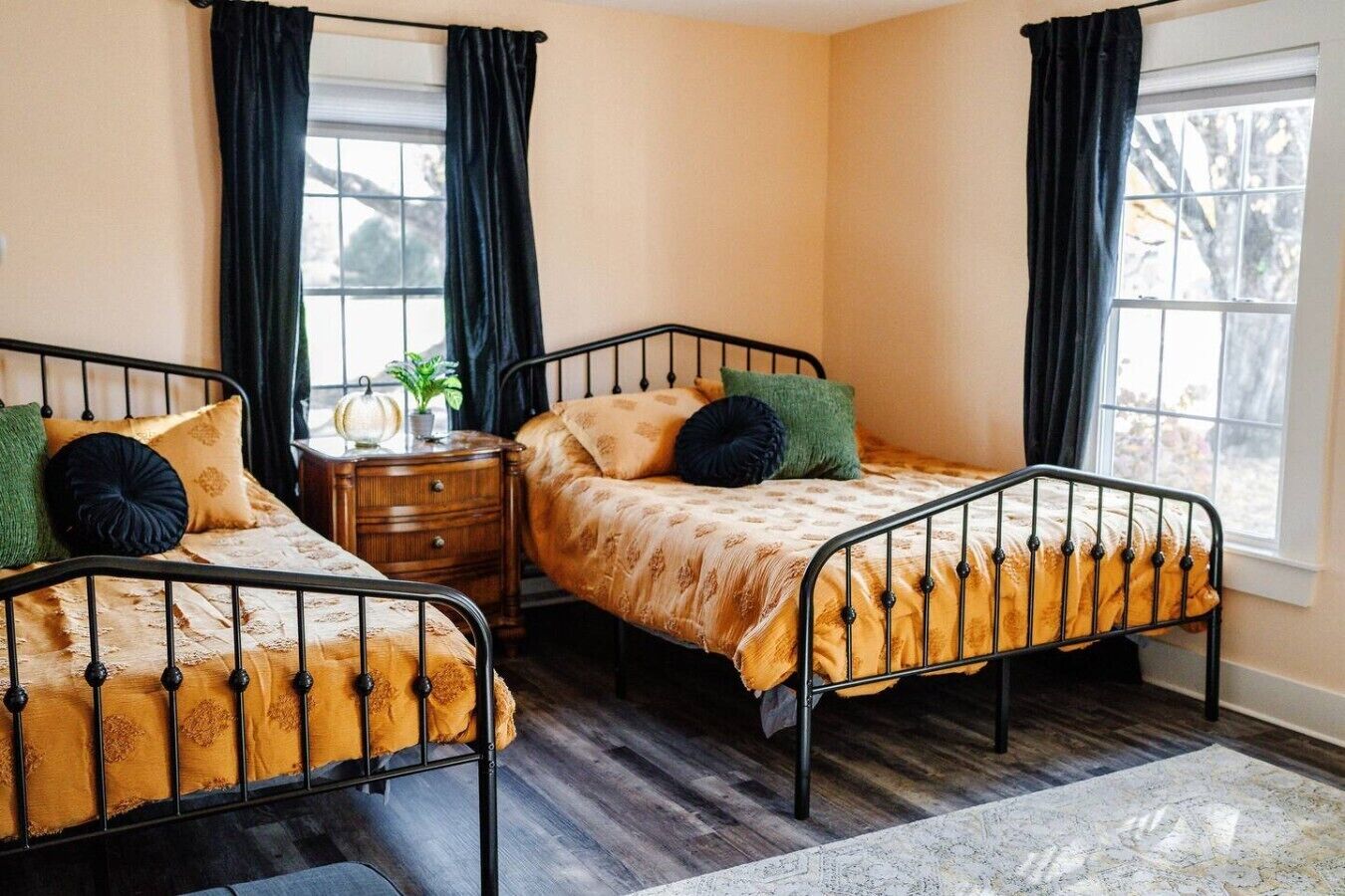 A room with two metal beds, a wooden nightstand, and a window with curtains.