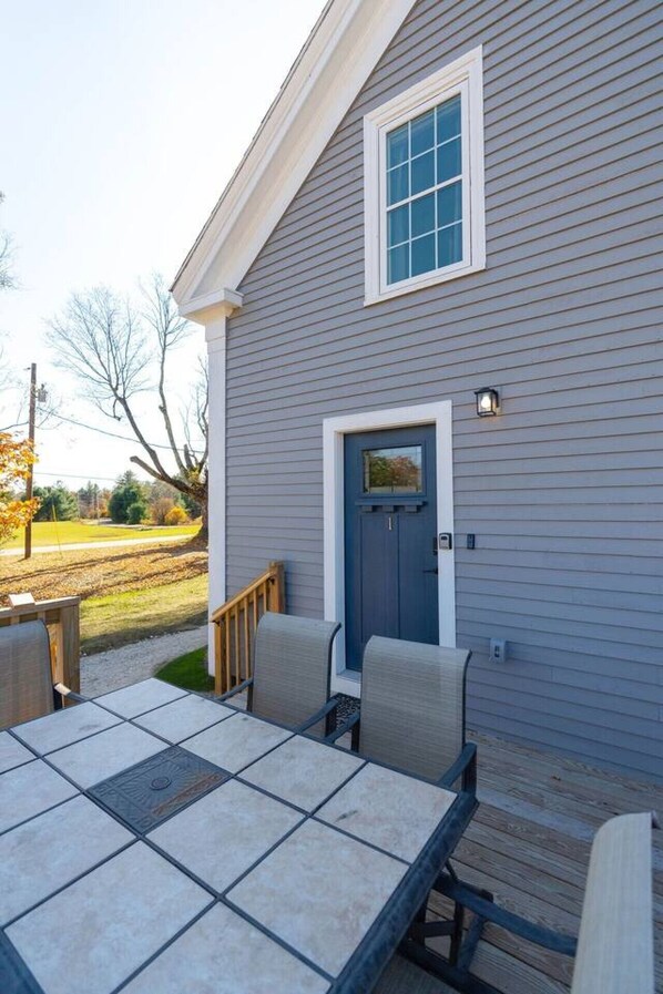 A house with a blue door, a small porch with a table and chairs, and a window above the door.