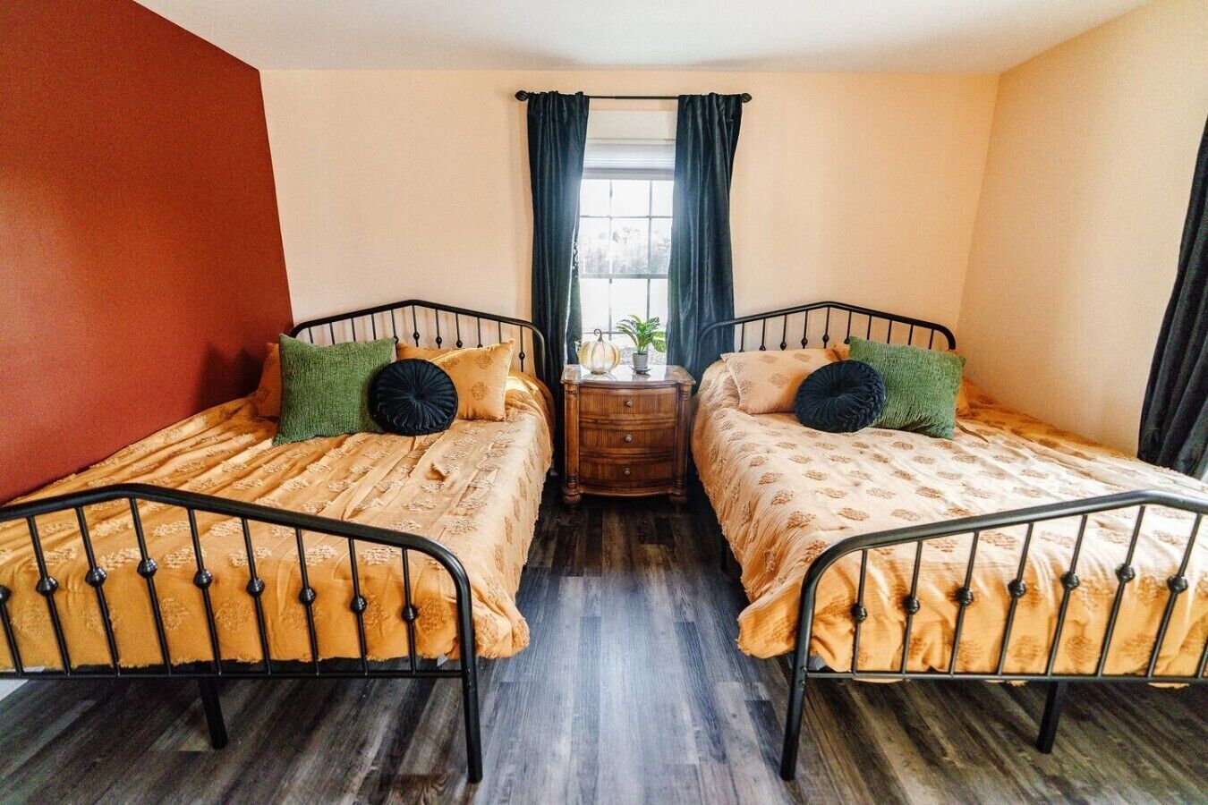 A room with two beds, a wooden nightstand, a window with curtains, and a potted plant.
