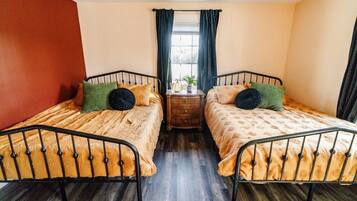 A room with two beds, a wooden nightstand, a window with curtains, and a potted plant.