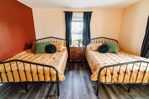 Una habitación con dos camas, una mesita de noche de madera, una ventana con cortinas y una planta en maceta.