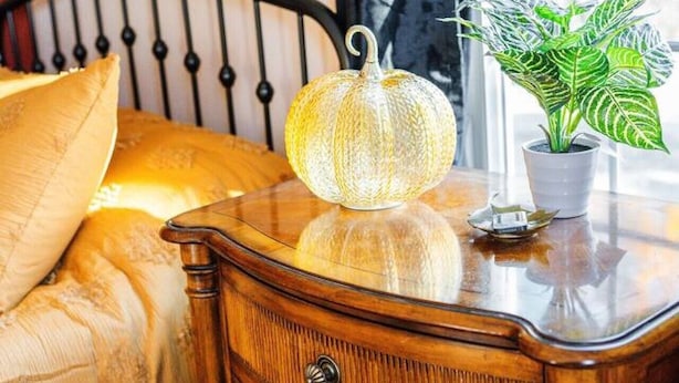 Une table de chevet en bois avec une lampe, une plante en pot et un lit avec une tête de lit.