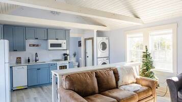 A spacious living area with a brown leather sofa, a kitchen with blue cabinets, and a ceiling fan.