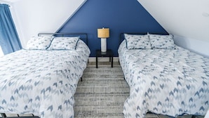 Una habitación con dos camas, una mesita de noche con lámpara y una pared de acento azul.