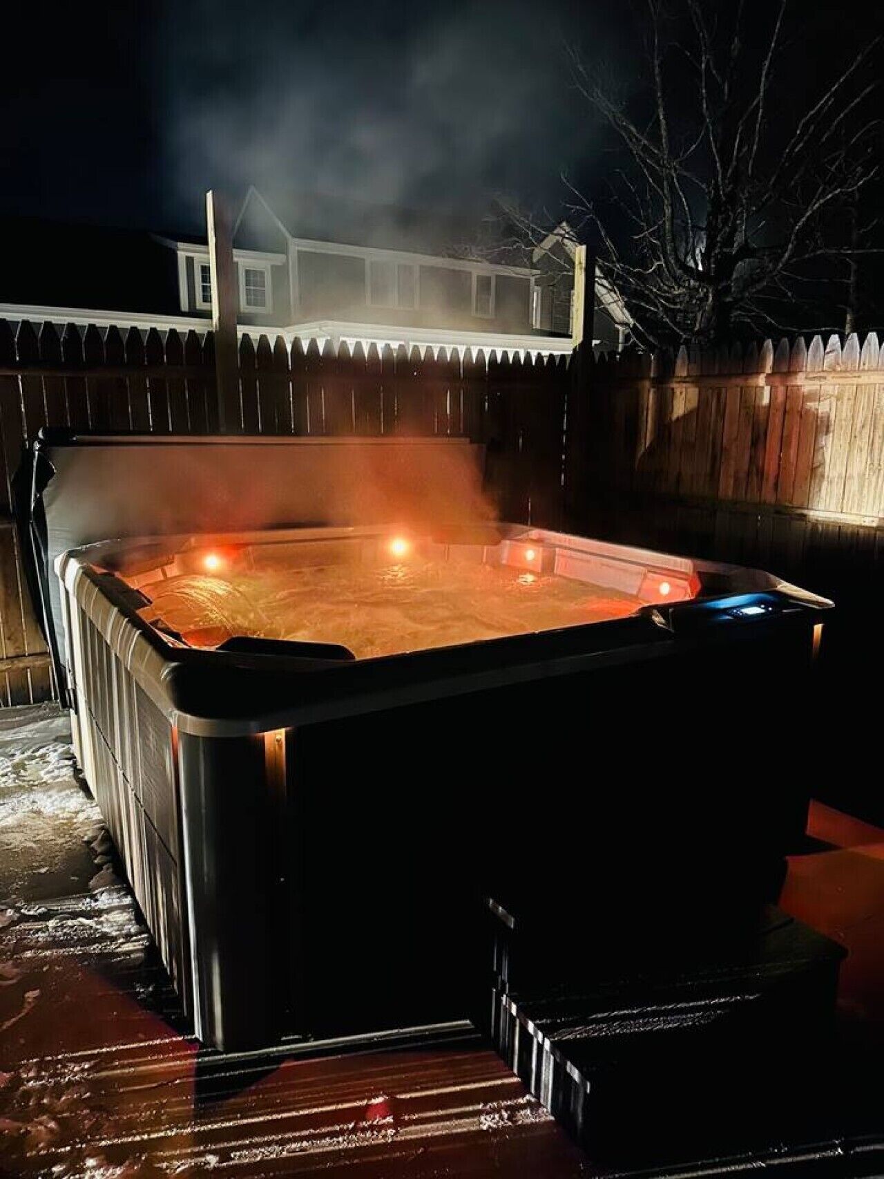 A hot tub outdoors with a wooden fence and a house in the background.