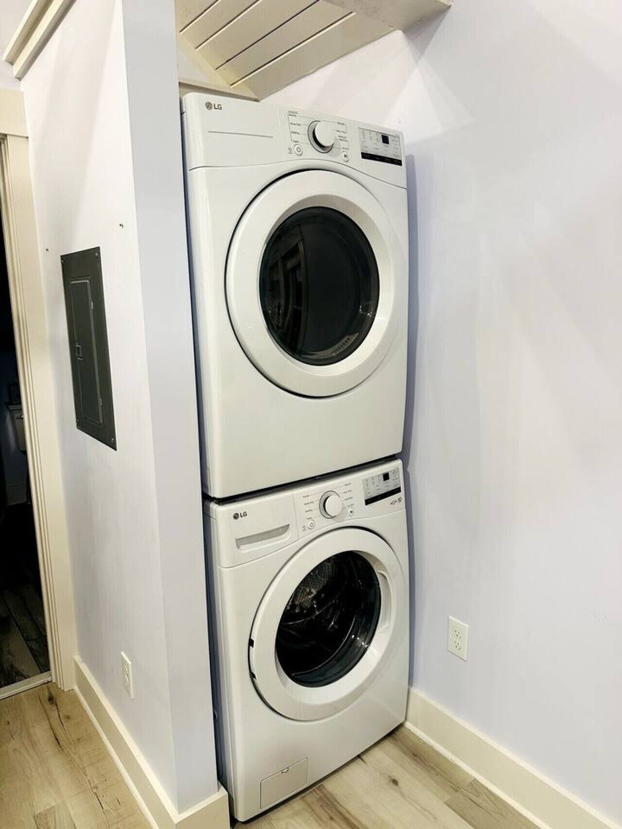 A stacked washer and dryer unit in a room with light-colored walls and wooden flooring.