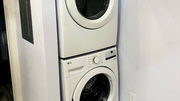 A stacked washer and dryer unit in a room with light-colored walls and wooden flooring.