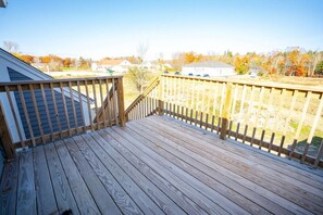 A wooden deck with a railing, leading to a residential area with houses and trees.