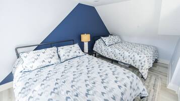 A bedroom with two beds, a blue accent wall, and a lamp.