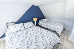 A bedroom with two beds, a blue accent wall, and a lamp.