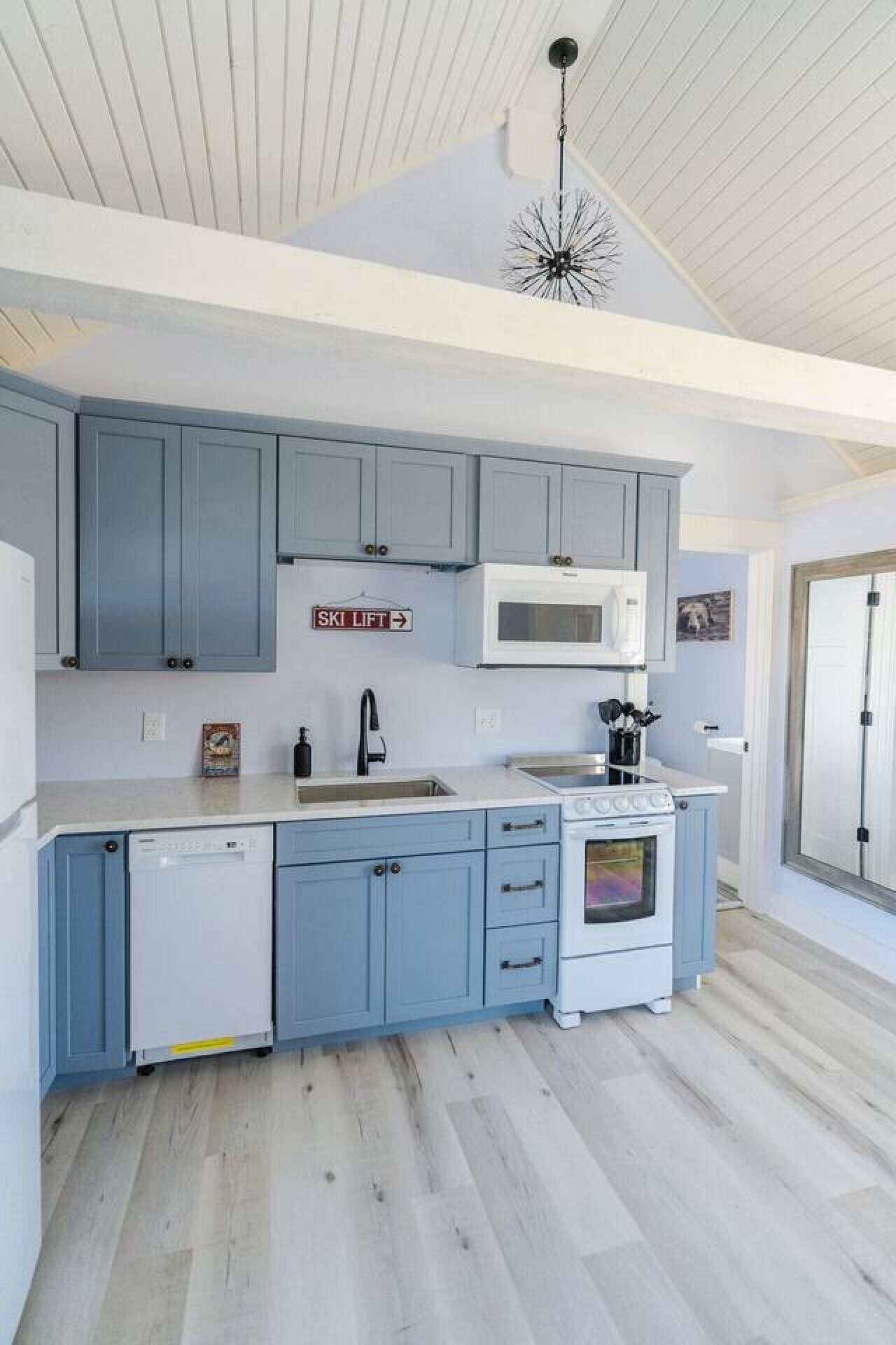 A modern kitchen with blue cabinets, a white microwave, and a dishwasher.